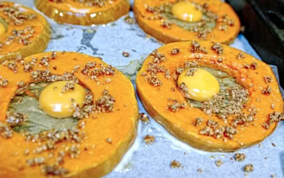 Pak jsem dýni vyndala z trouby ven a do každé díry rozklepla 1 celé vejce. Datle a ořechy jsem rozmixovala na drobenku v mixéru a posypala jimi všechna dýňová kolečka. Vejce jsem ještě lehce dosolila a opepřila. Na závěr jsem vše dokořenila medvědím česnekem. Pekla jsem dalších 20 minut při 200°C.