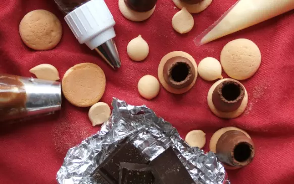 - do zdobícího sáčku dejte nástavec na špičky, ustřihněte spodek sáčku a špejlí nebo něčím ostrým udělejte do sáčku díru v místech, kde je postranní otvor ve zdobičce - díky téhle dírce bude mít formička dostatek vzduchu, aby mohly vznikat špičky tak, jak mají

- asi 1/6 krému si dejte stranou na uzavření špiček

- menší část čokoládového krému přendejte do sáčku - nedávejte si ho tam příliš, protože krém se při plnění dost rychle ohřívá v ruce a pak s ním jde špatně pracovat

- na připravené piškoty nastříkejte "trubičku", když chcete tunýlek ukončit, pohněte sáčkem lehce na jednu stranu, krém se vám "odlomí"